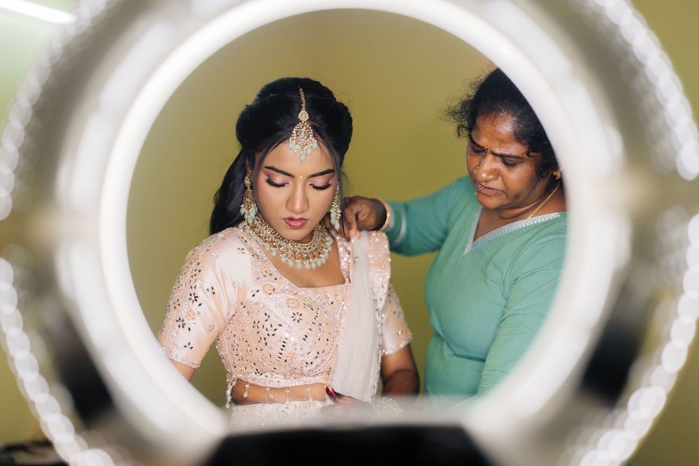 Close-up view through a decorative frame showing traditional Indian bridal preparation and makeup application.
