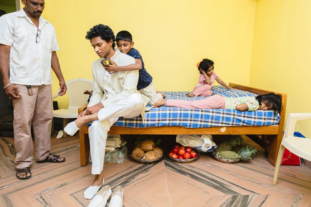People relax in a room with a bed, watermelon, and other fruits on the floor against a yellow wall.