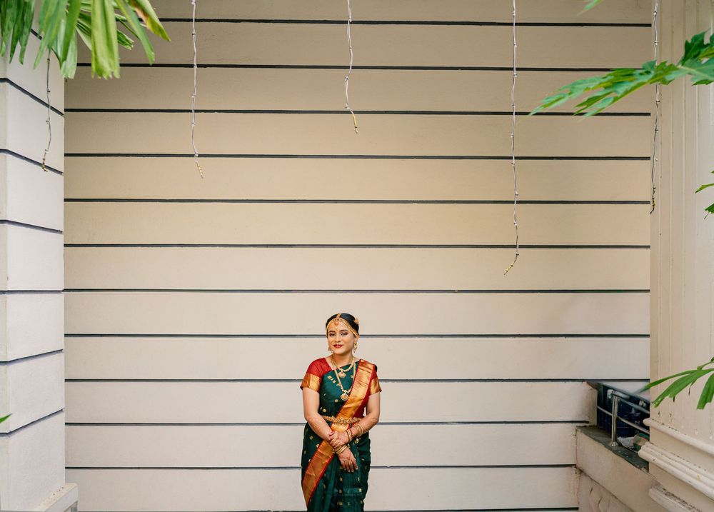 Bride in traditional South Indian attire standing against slatted wall with plants.