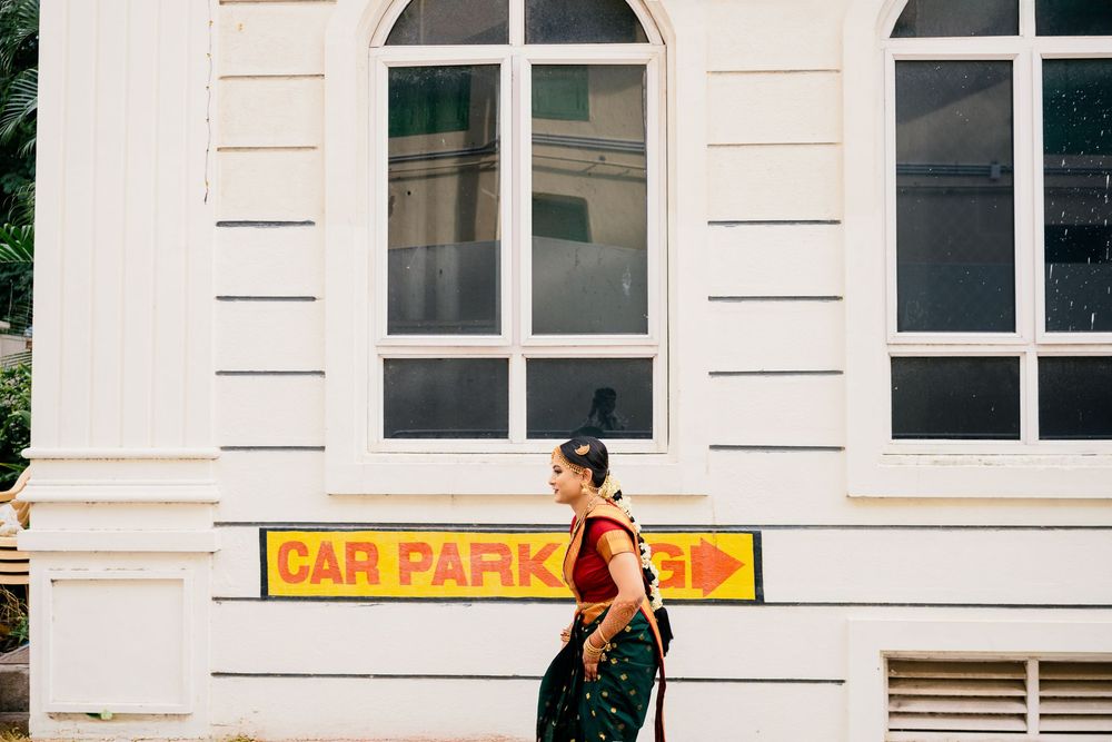 A person in black clothing walks past a white building with arched windows and a car park sign.