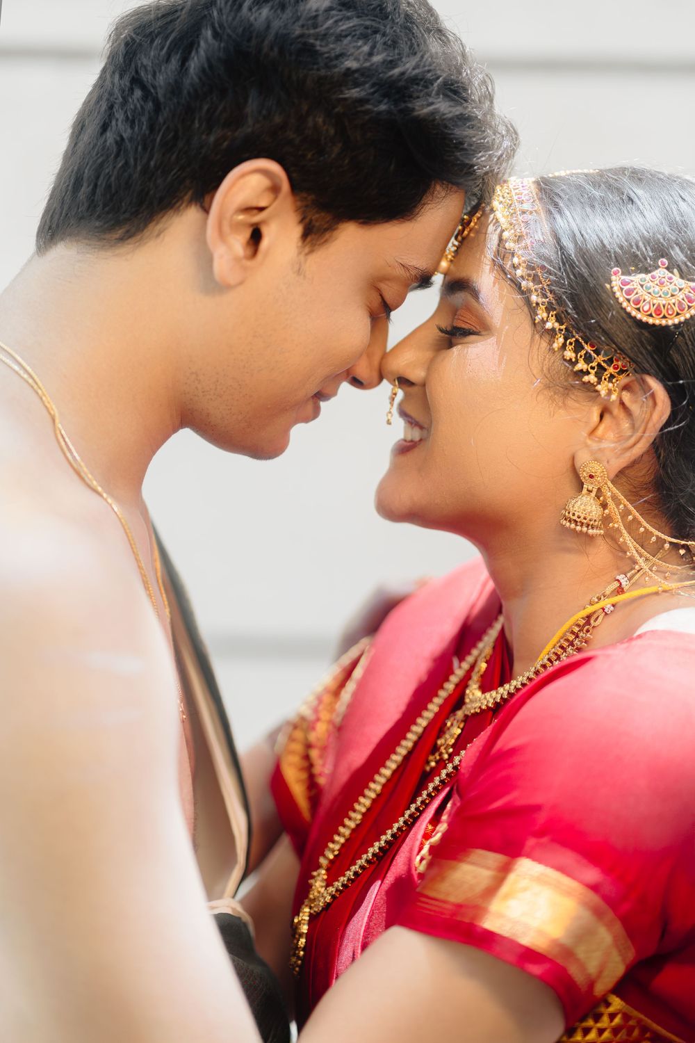 A couple in South Asian wedding attire share a tender moment against a light background.