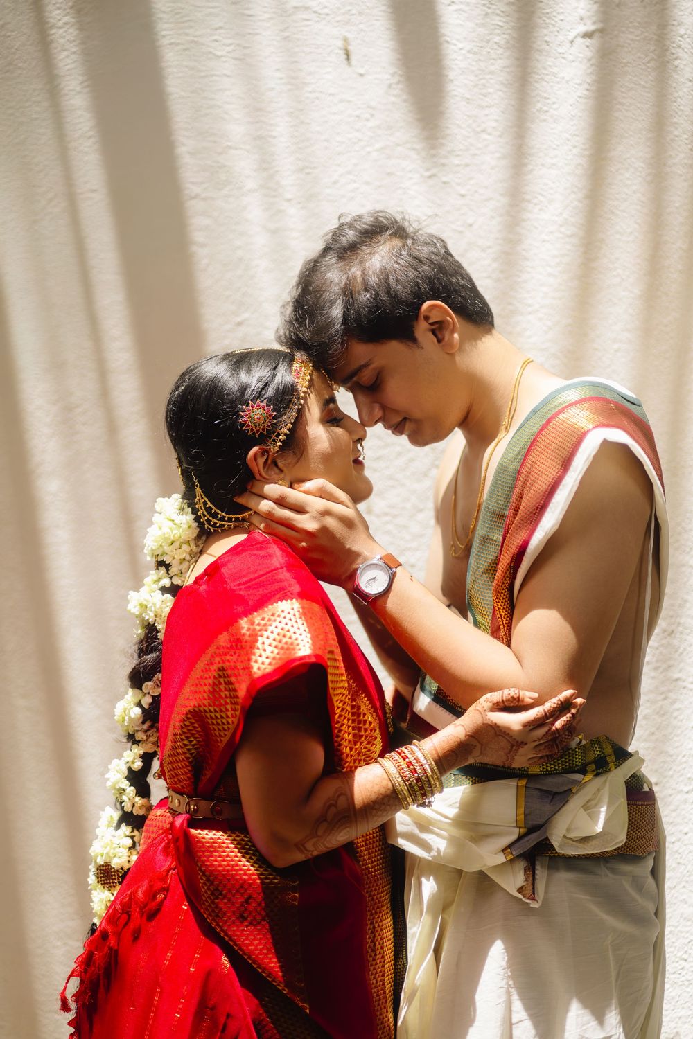 Intimate moment between couple in traditional South Asian wedding attire against white backdrop.
