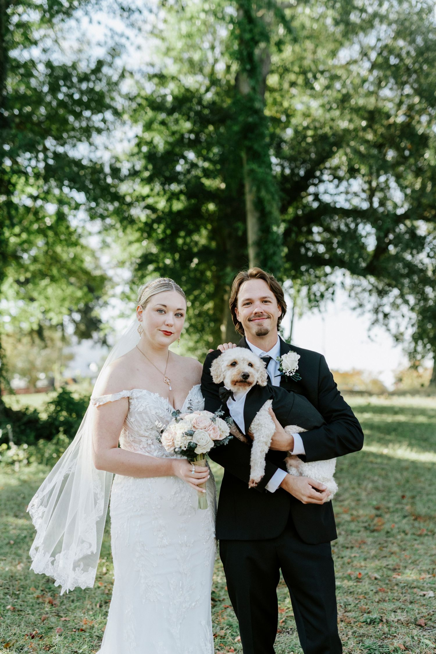 A couple in wedding attire shares joyful moments with their small dog during an outdoor photo session.