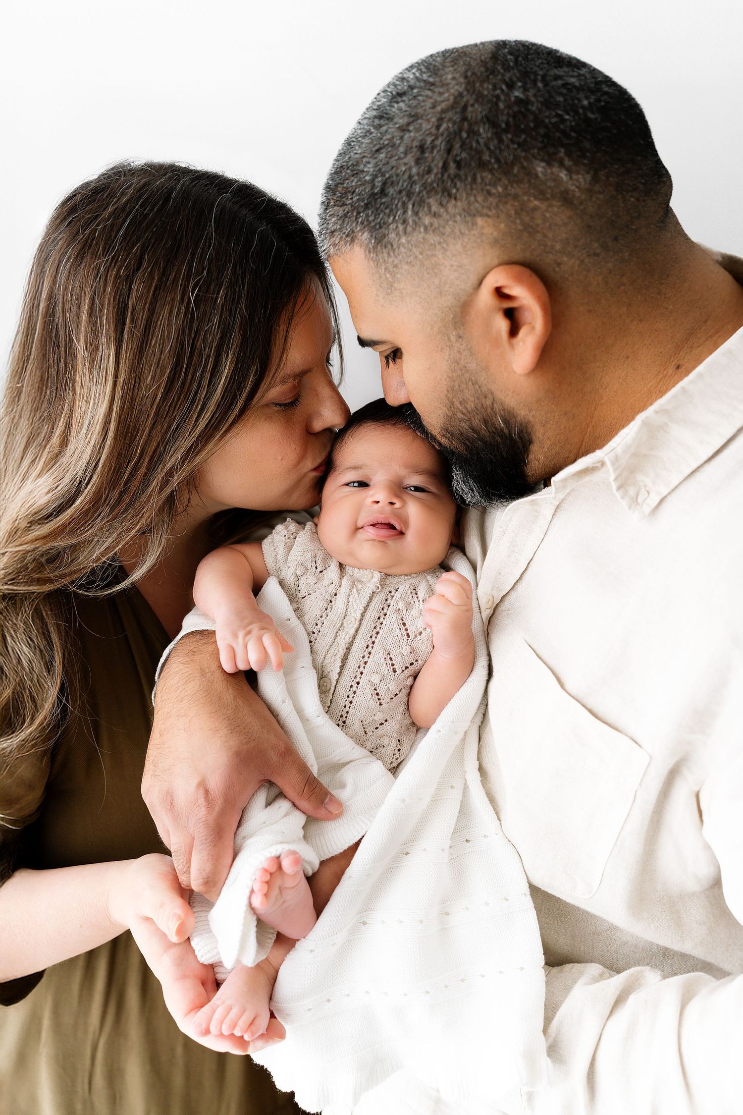 A series of intimate family photos showing tender moments between parents and baby in soft white and neutral tones.