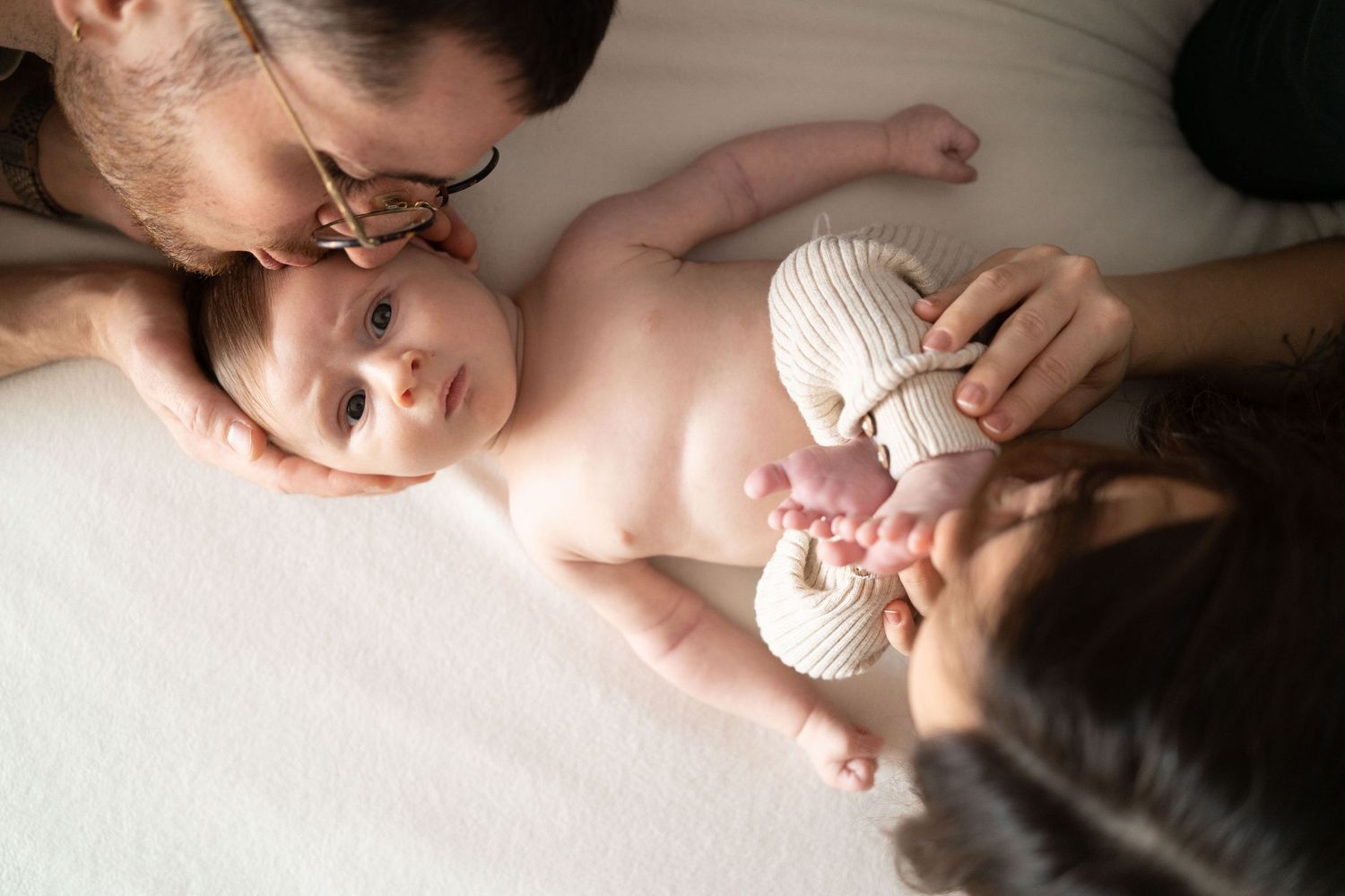papà bacia la fronte di neonato, mamma bacia i piedini di neonato