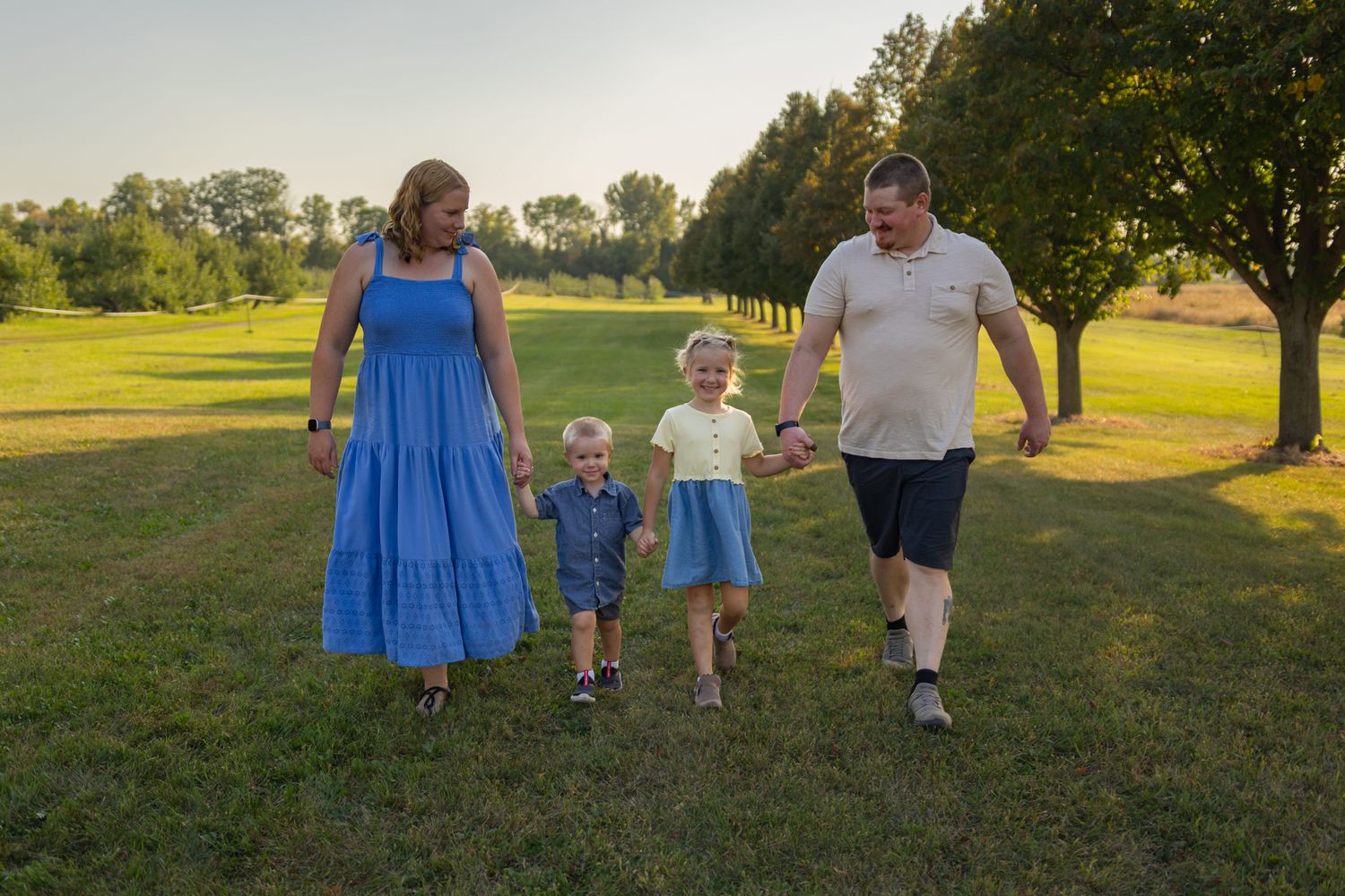 A family in coordinated blue and white outfits poses together in a sunny field during golden hour.