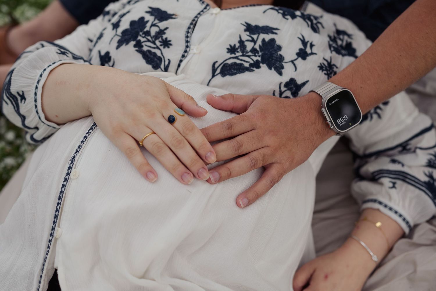 Expecting mother’s belly with her hand and her husband’s hand resting on it.