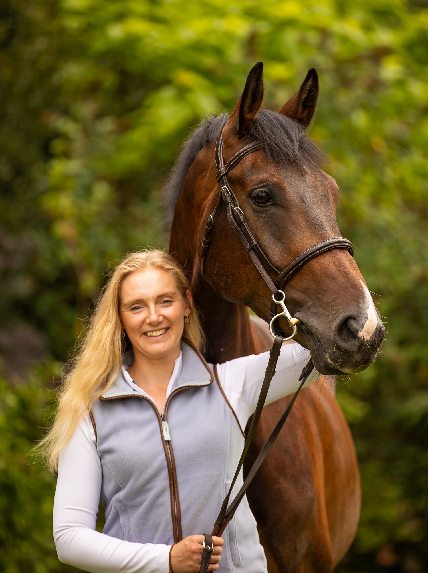 A large cream-colored draft horse and its companion pause together in a sunlit autumn forest.
