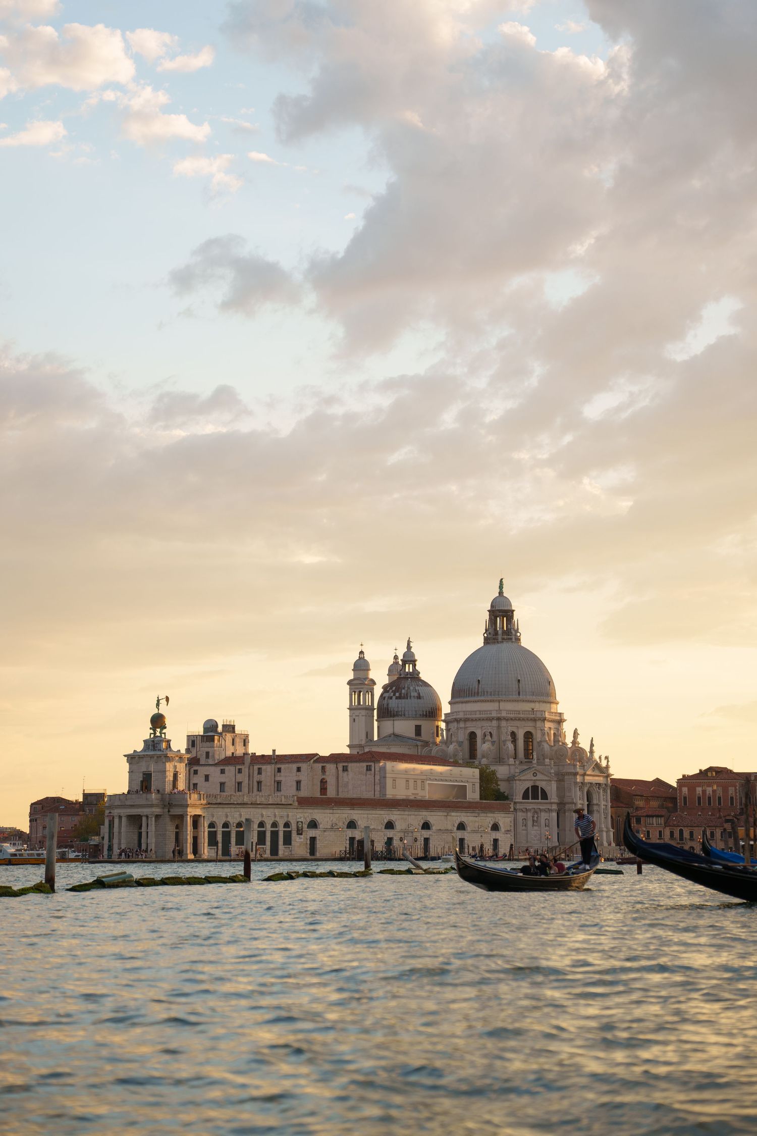 Panoramic view of Venice's historic skyline with Santa Maria della Salute church and gondolas at sunset over rippling waters.