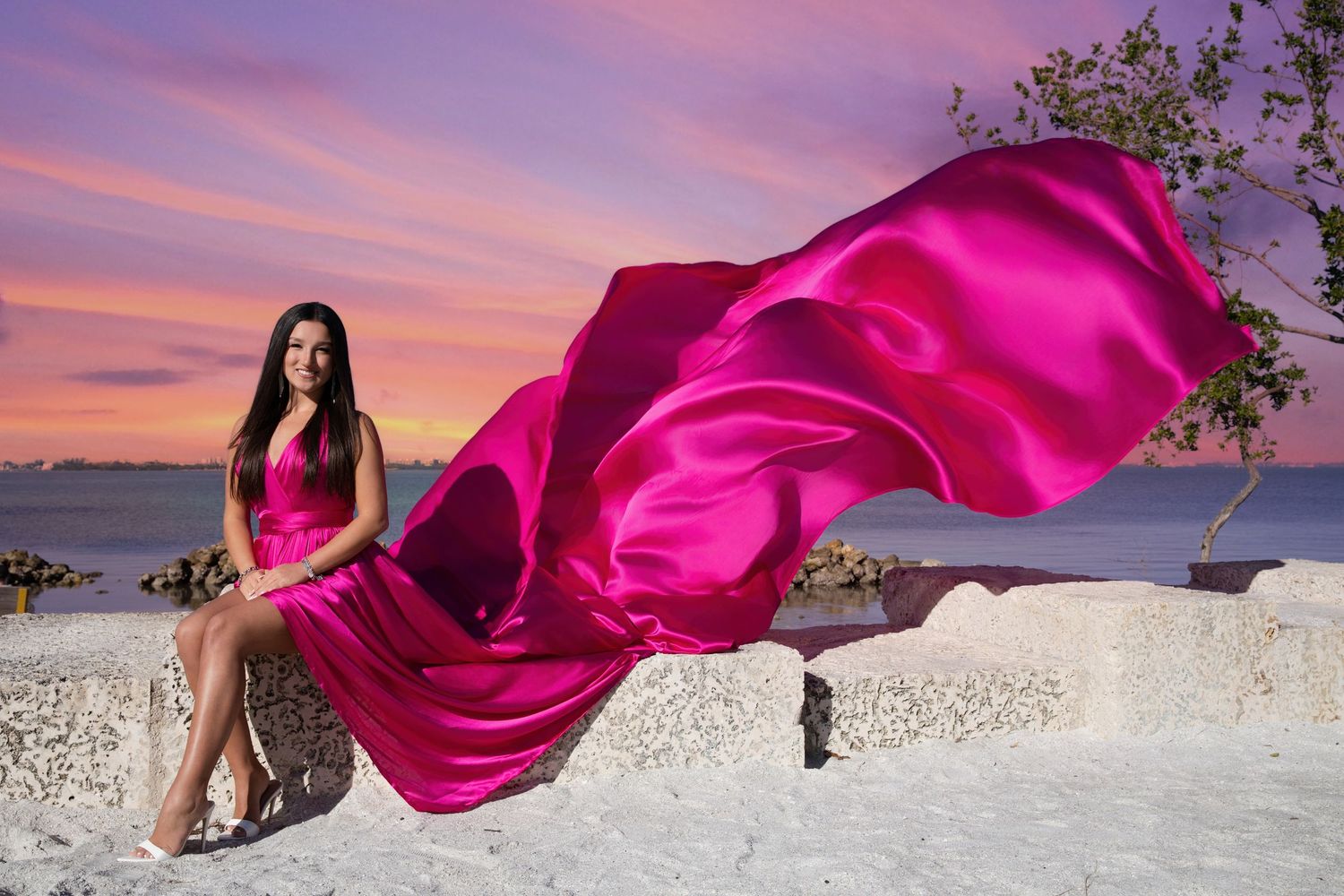 A flowing magenta dress billows dramatically against a white sand beach and pink sunset sky. Flying Dress Photoshoot