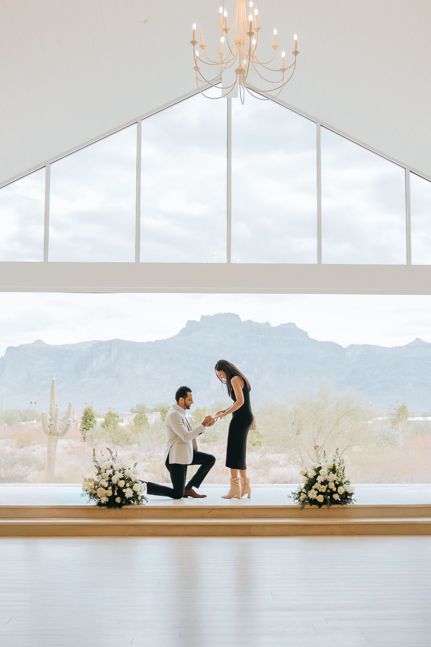 Marriage proposal moment in modern white chapel with chandelier and mountain views.
