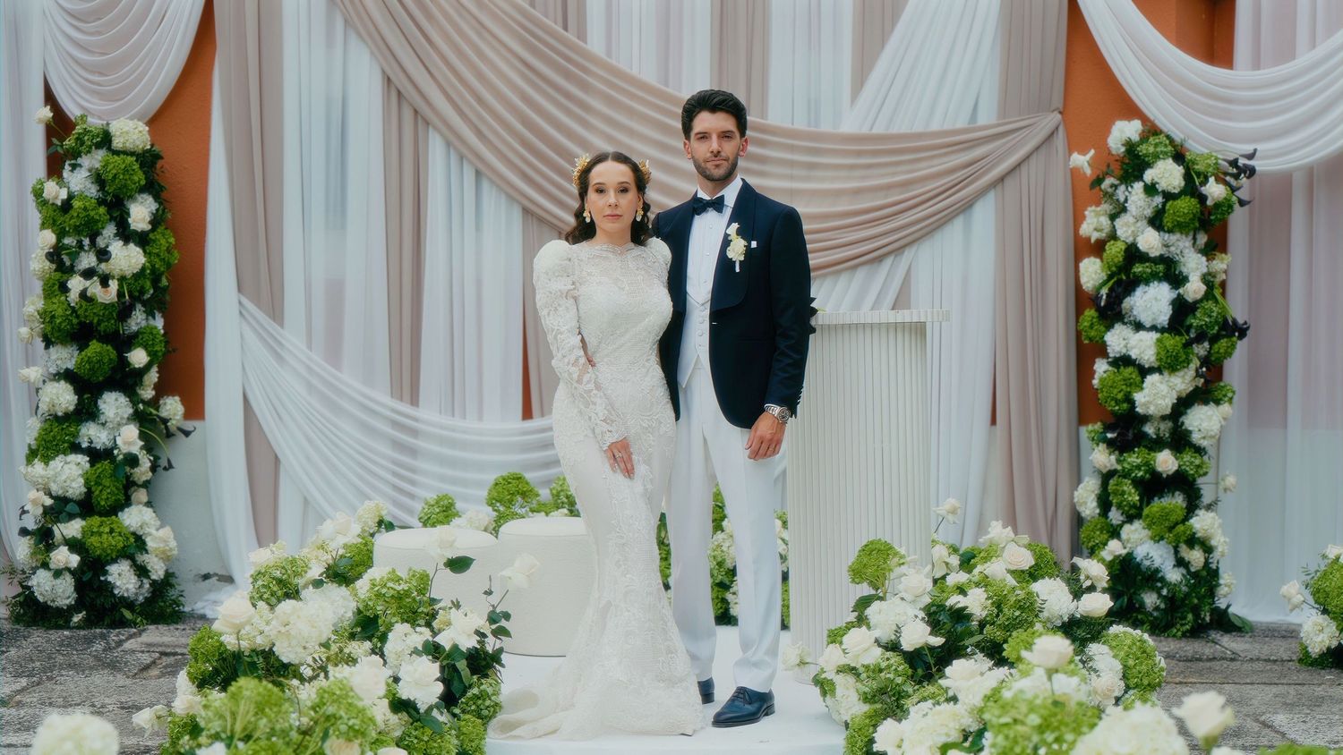 An elegant wedding ceremony setup with white floral arrangements and draped fabric creating a romantic backdrop.