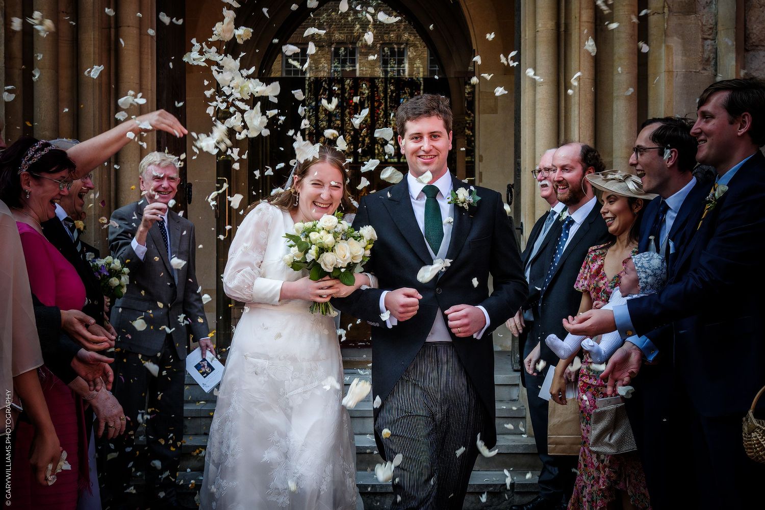 Wedding couple exits church ceremony while guests throw confetti and petals in celebration at traditional ceremony.