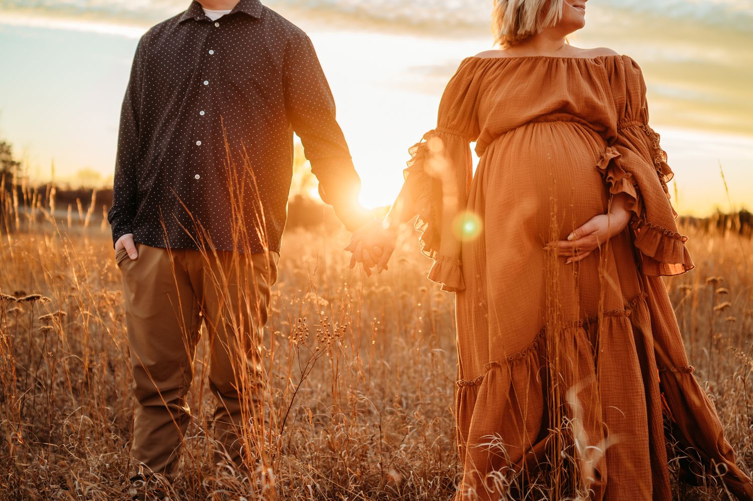 Couple sitting together on grassy hill during golden sunset near rustic fence.