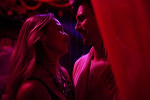 Two people in close proximity under dramatic red lighting creating an intimate mood.