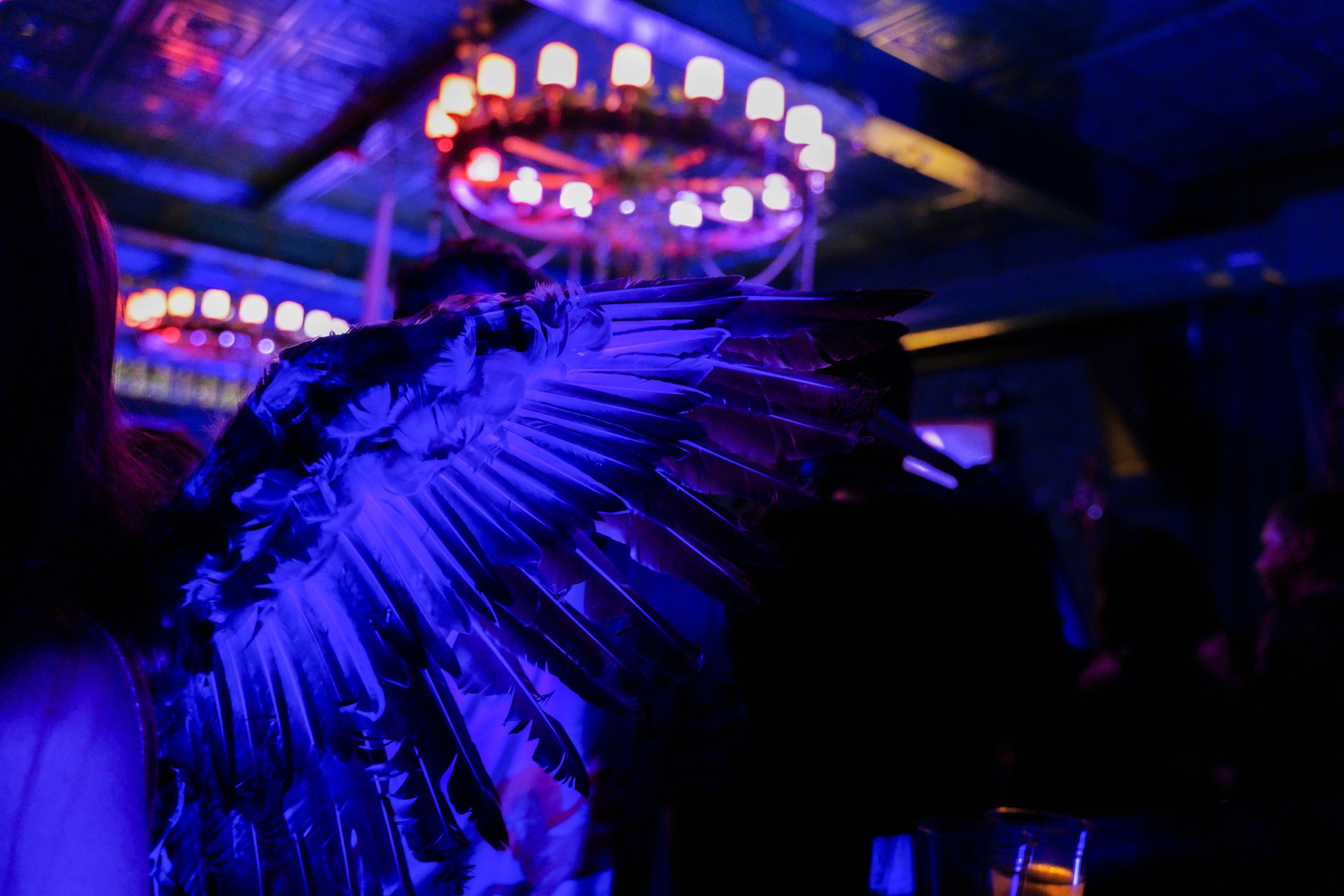 Ornate chandelier casts blue light across a dark nightclub ceiling with decorative patterns.