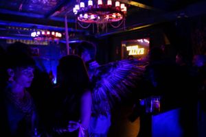 Dark nightclub interior illuminated by circular chandeliers with silhouetted crowd below.