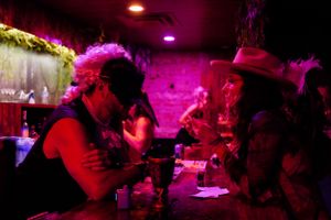 Pink-tinted nightclub scene with patrons gathered at a dimly lit bar.