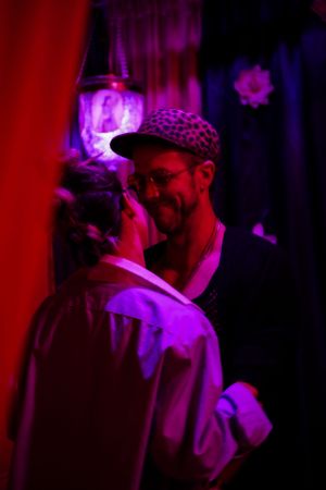 Nightclub scene bathed in purple lighting with silhouetted figures in conversation.