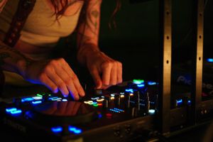 Close-up of hands adjusting controls on a DJ mixer with glowing blue LED lights.