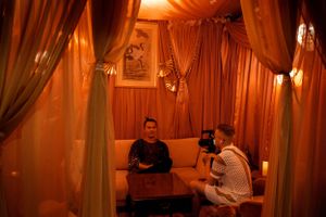 Two people having a private conversation in an intimate lounge setting with warm amber lighting.