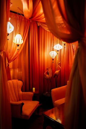 Cozy lounge area with orange drapes, glowing paper lanterns, and plush seating.