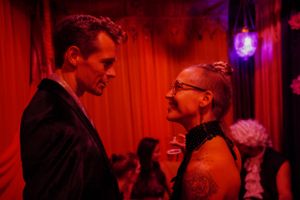 Two figures engaged in conversation under dramatic red lighting at a social event.