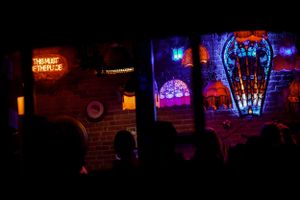 Dark nightclub interior with glowing neon signs and silhouetted figures.