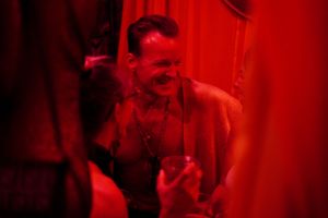 Intimate bar scene bathed in deep red lighting with dramatic shadows.