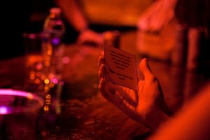 Close-up shot of hands holding a menu card under dim red lighting at a bar.