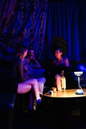A group socializes at a dimly lit lounge with blue lighting and decorative curtains.