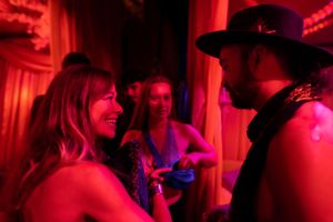 Nightclub scene bathed in red lighting with patrons enjoying conversation.