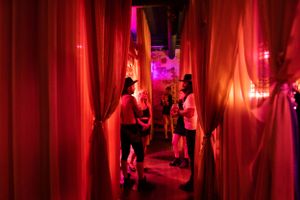 Red-lit hallway with flowing curtains and people walking through.