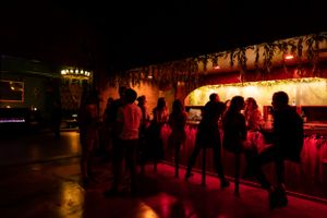 Silhouettes of people gathered at a bar under moody red lighting.