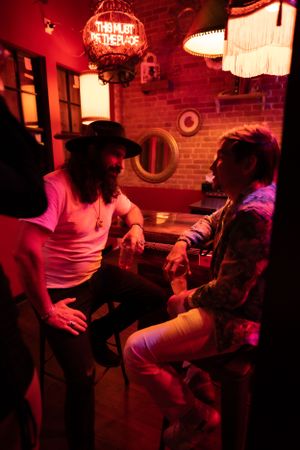 Two people in conversation under red neon lighting at a bar.
