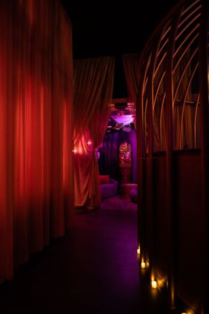 Dramatic red-curtained hallway with purple backlighting and floor candles.