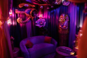 Dimly lit lounge area with purple lighting, curved sofa, and Egyptian-themed decor featuring hanging dragon sculptures.