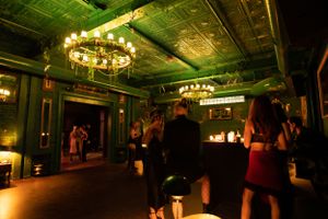Vintage ballroom with ornate ceiling, chandeliers, and green atmospheric lighting.