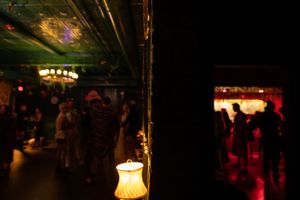 Dimly lit nightclub interior with vintage lamp and silhouetted crowd.
