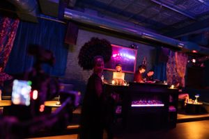 Dark moody bar setting with neon lights and silhouetted figures.