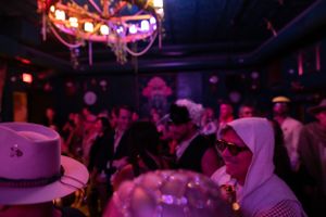 Nightclub patrons enjoy a crowded dance floor under purple and red lighting with decorative overhead fixtures.