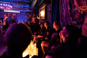 Nightclub patrons seated at tables under moody lighting with glowing signage in background.