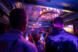 Crowd enjoying nightclub atmosphere beneath ornate ceiling fixtures with purple lighting.