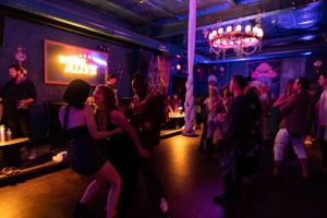 Energetic dance floor scene with neon signs and dramatic lighting creating party atmosphere.