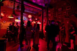 Crowded nightclub with red neon lighting and people mingling on the dance floor.