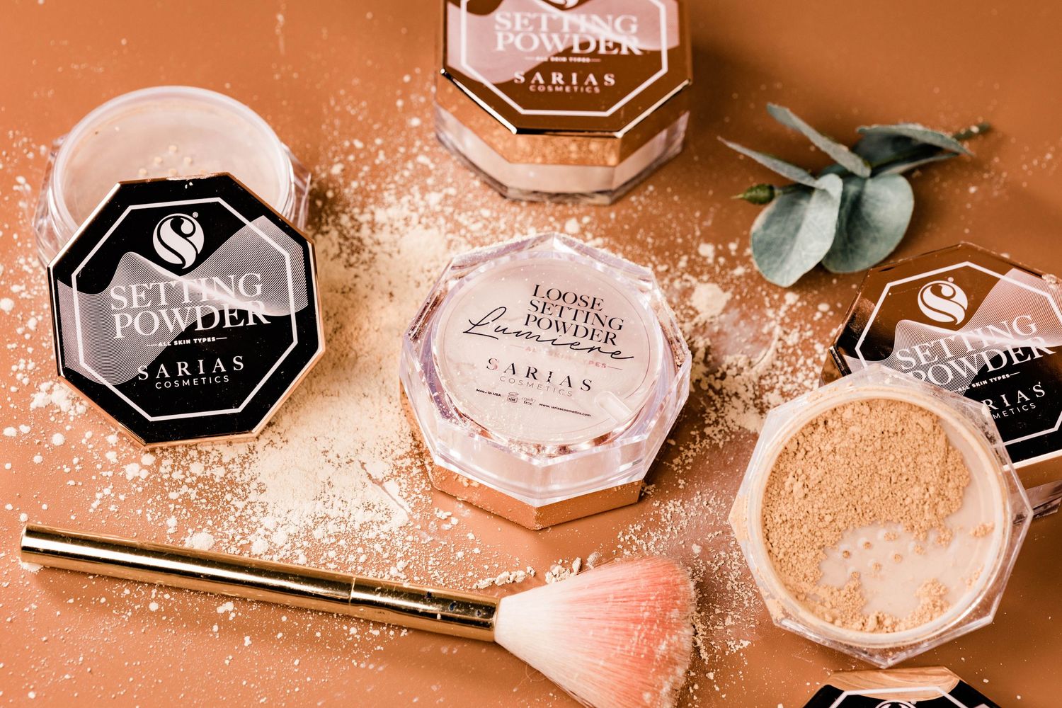 Makeup products including powder compacts and a pink makeup brush arranged on a coral background.
