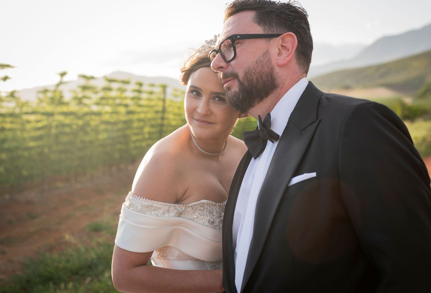 A couple shares an intimate moment together at sunset in a vineyard with rolling hills in the background.