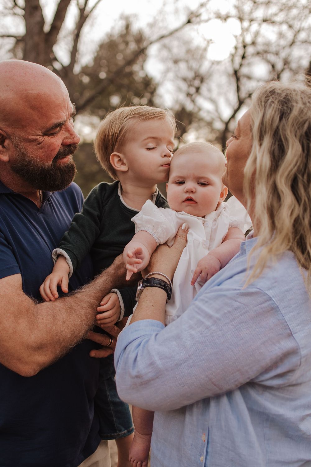 A tender family moment outdoors as parents hold and interact with their young children. Dallas Texas