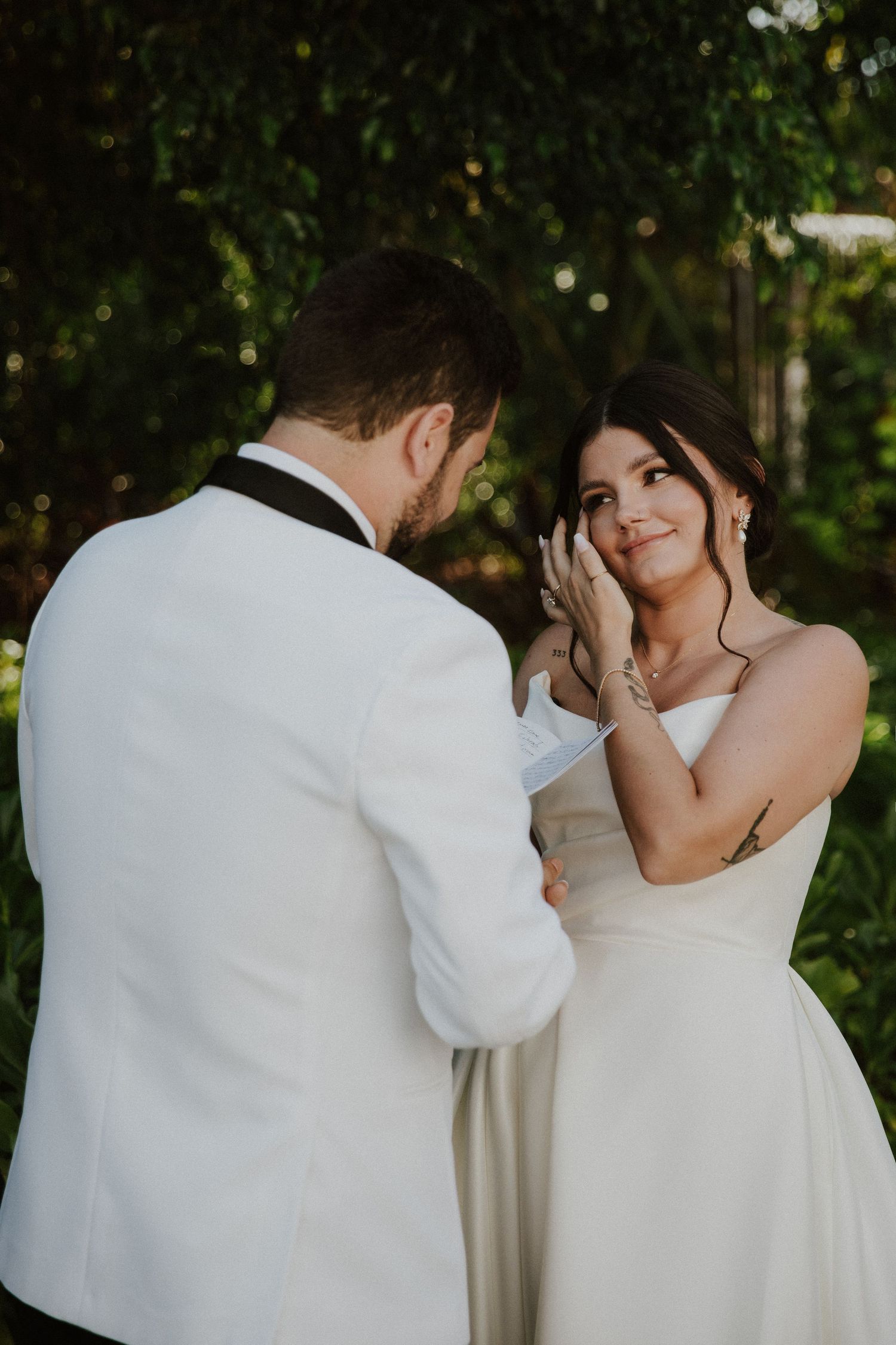 A romantic moment between a couple in white attire dancing together in a garden setting with lush greenery.