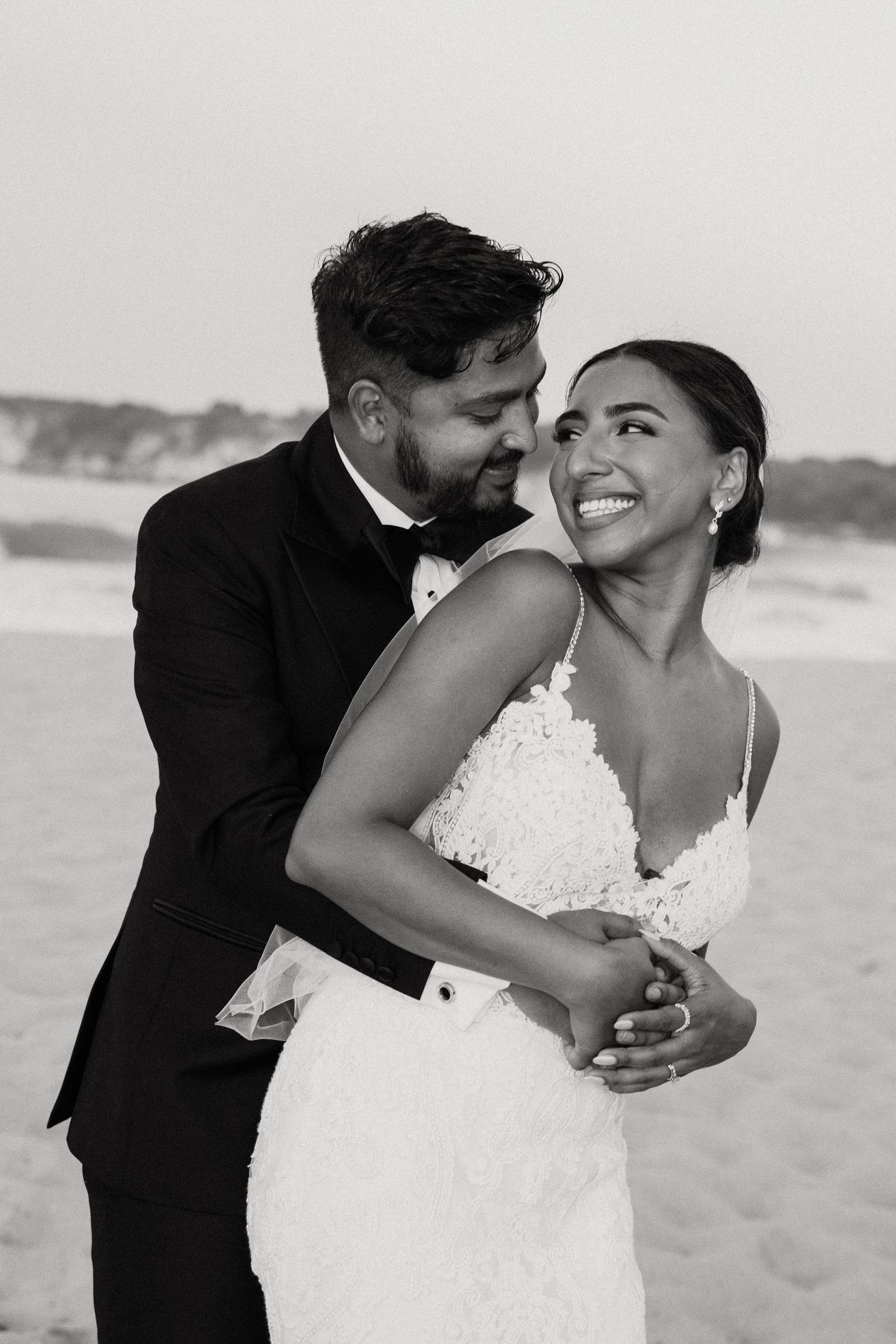 Black and white beach wedding portrait capturing candid laughter between newlyweds.